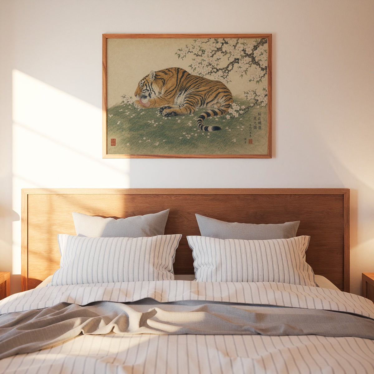Tiger resting under cherry blossoms print in a warm wood frame above a bed with striped linen bedding