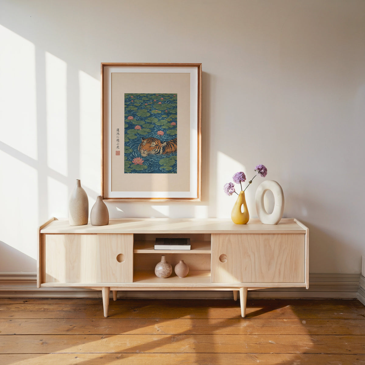 tiger swimming in lotus pond print shown in a wood frame with a white mat above a pale wood media console