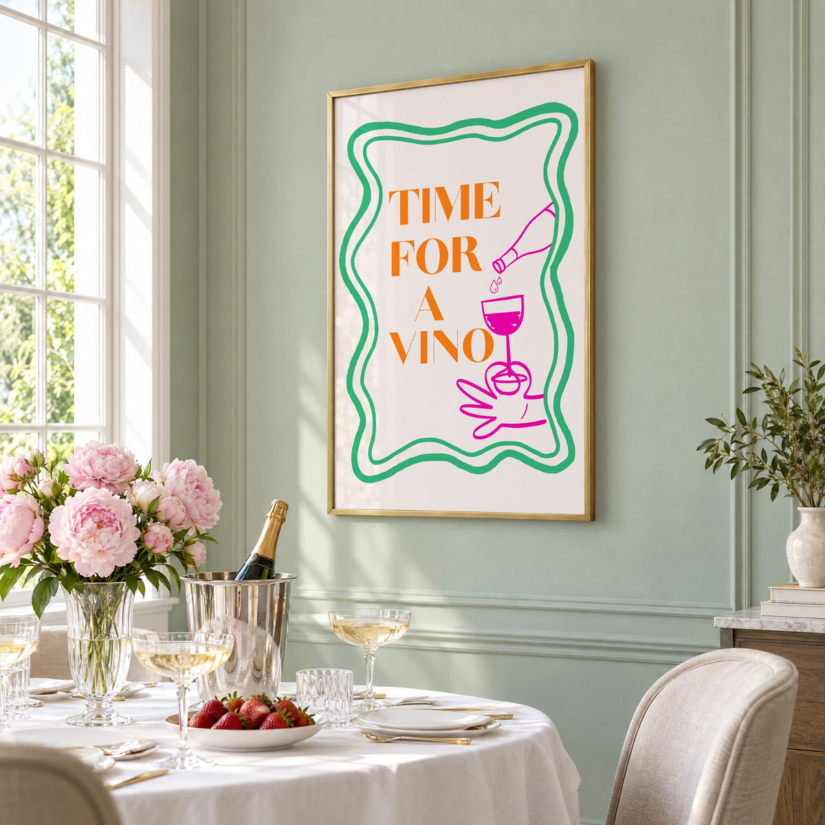TIME FOR A VINO wine pour wavy frame print in a brass frame on a sage wall above a brunch table with champagne and peonies, seen at an angle