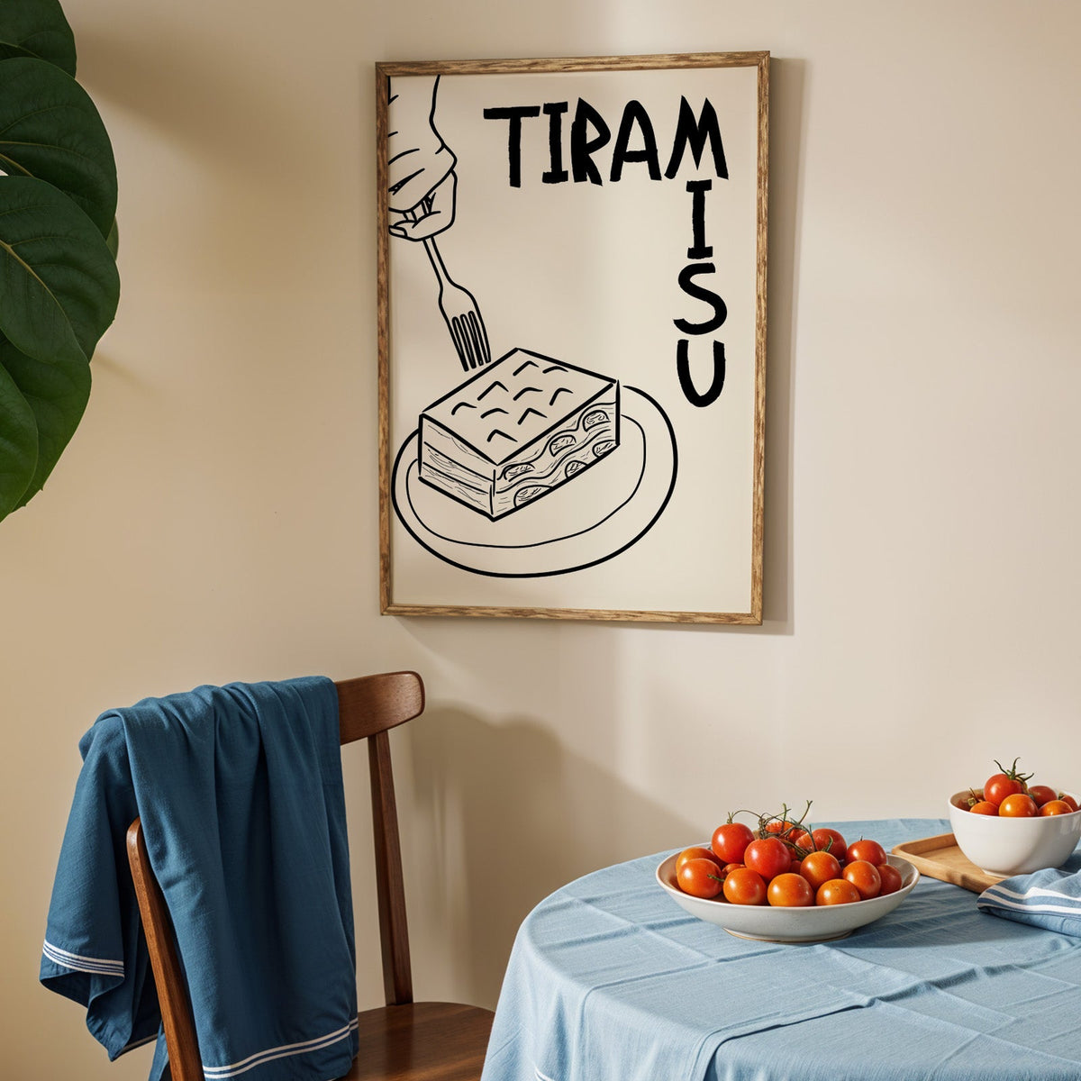 Tiramisu line art print in an oak frame above a blue linen table with ripe tomatoes
