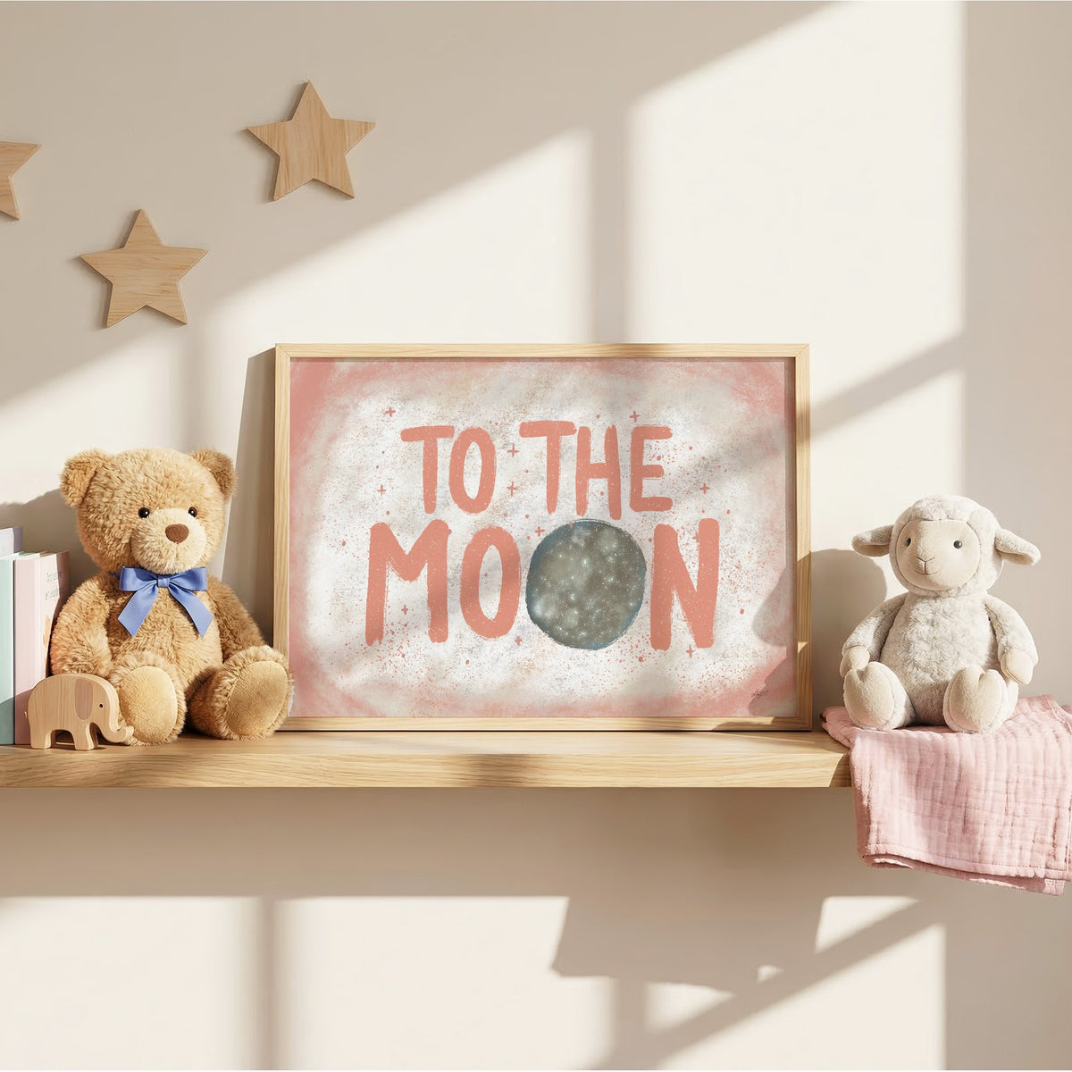 To the moon coral lettering nursery print in an oak frame on a wall shelf between a teddy bear and a toy lamb