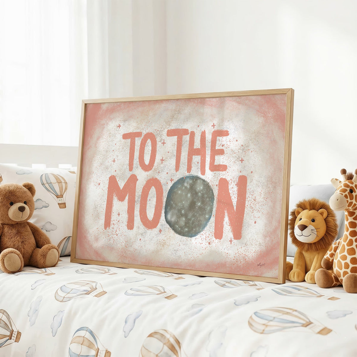 To the moon coral lettering nursery print in an oak frame on a kids bed with hot air balloon bedding