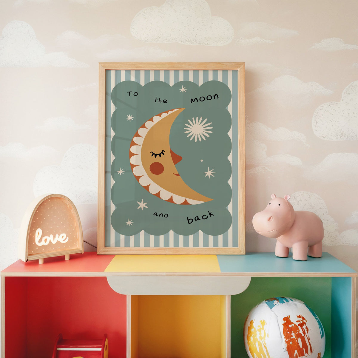 To the moon and back nursery print in an oak frame on a rainbow toy shelf against cloud wallpaper