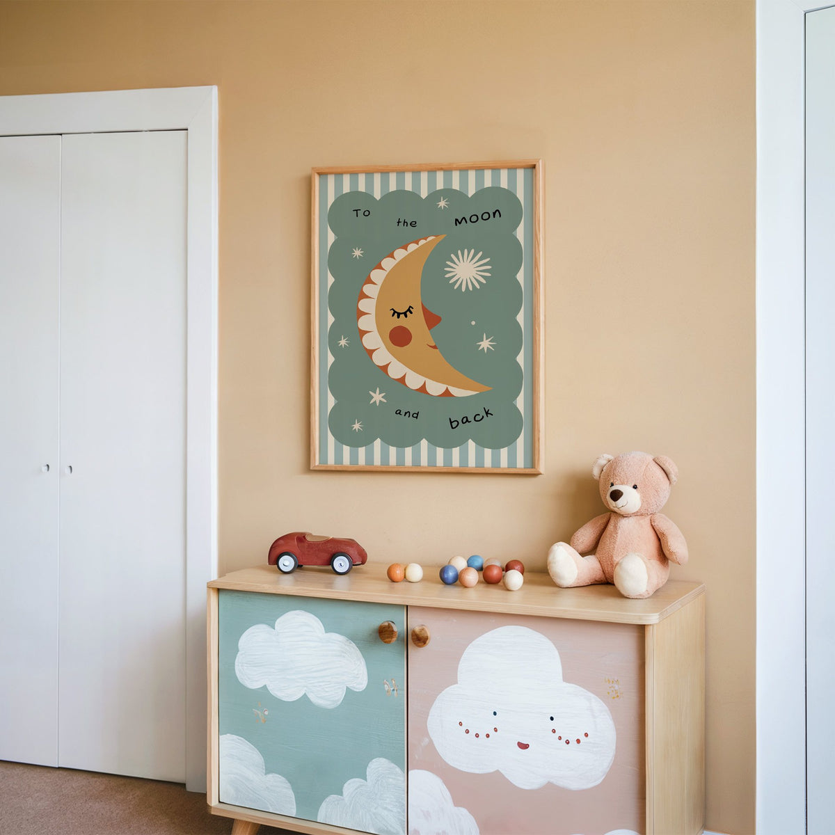 To the moon and back nursery print in an oak frame on a peach wall above a cloud-painted cabinet