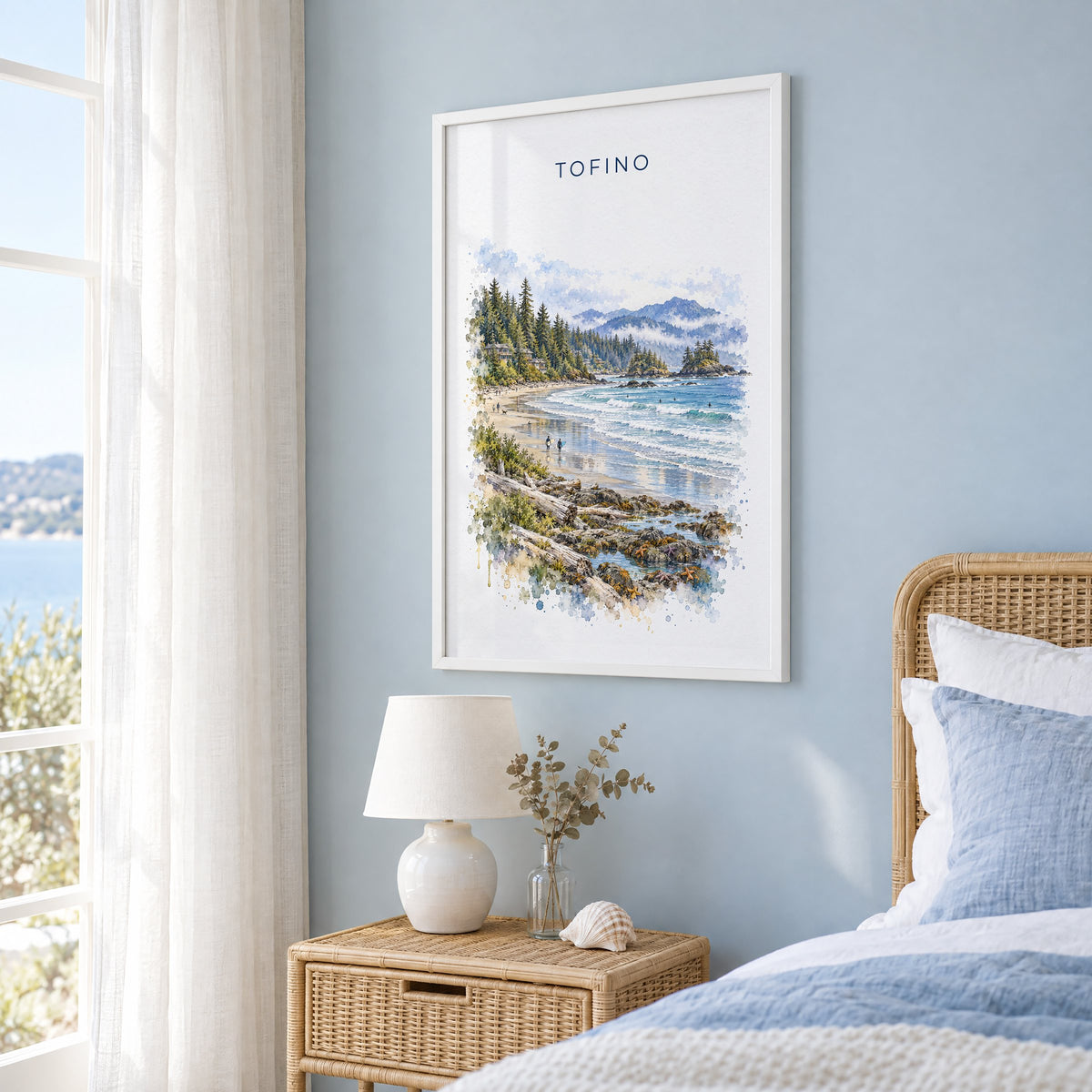 Tofino watercolor print in a white frame on a pale blue wall beside a rattan bed in a coastal bedroom