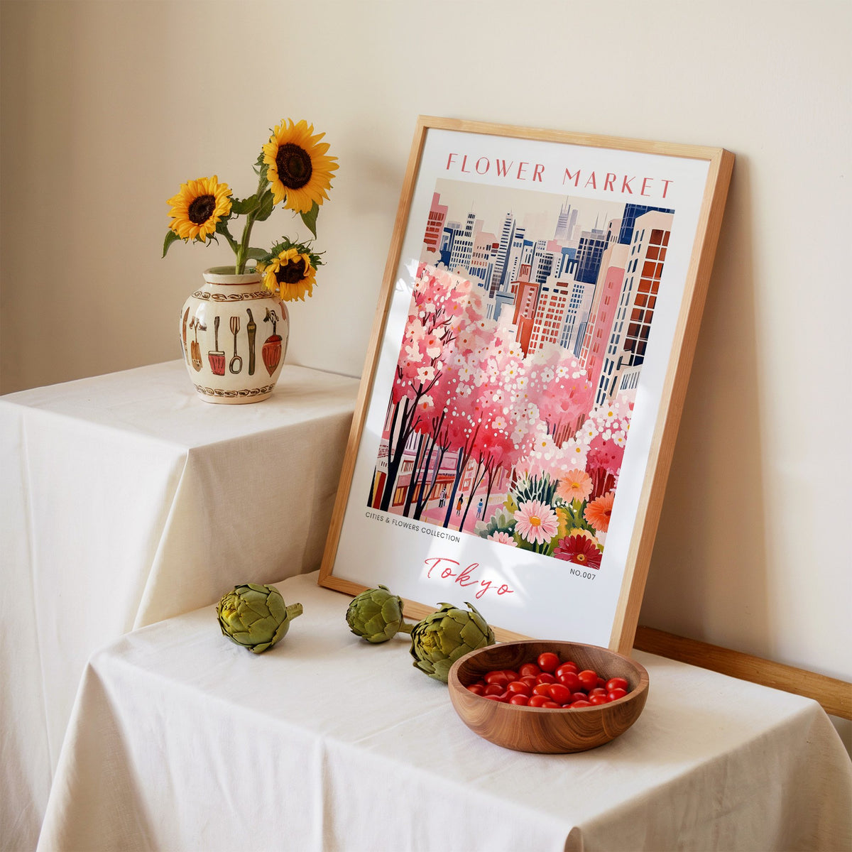 Tokyo flower market print in an oak frame leaning on a linen-draped table beside a vase of sunflowers