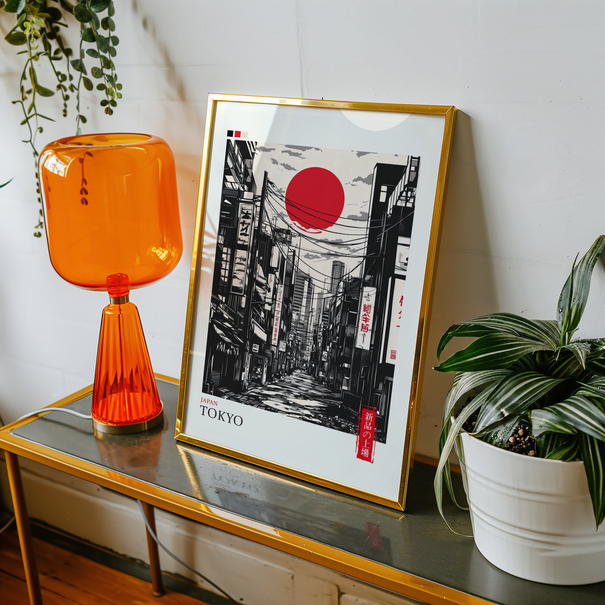 Tokyo ink street with red sun print shown in a gold frame on a console beside an orange glass lamp