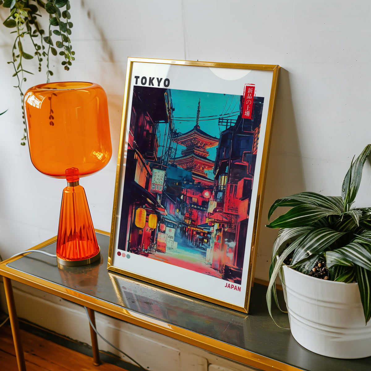 Tokyo neon alley and red pagoda print shown in a gold frame on a console beside an orange glass lamp
