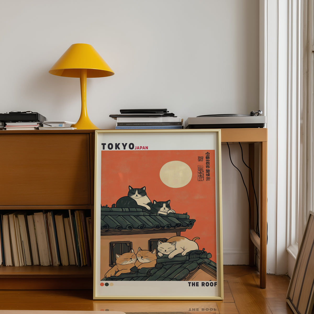 Five cats sleeping on Tokyo roof print shown in a gold frame below a teak desk with a yellow lamp
