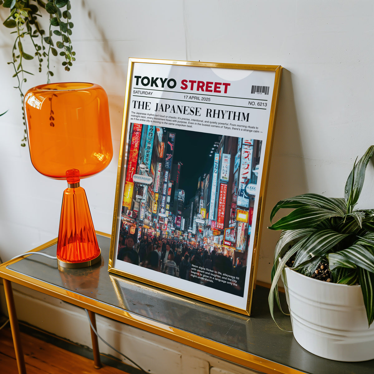 Tokyo street neon newspaper print shown in a gold frame on a console beside an orange glass lamp