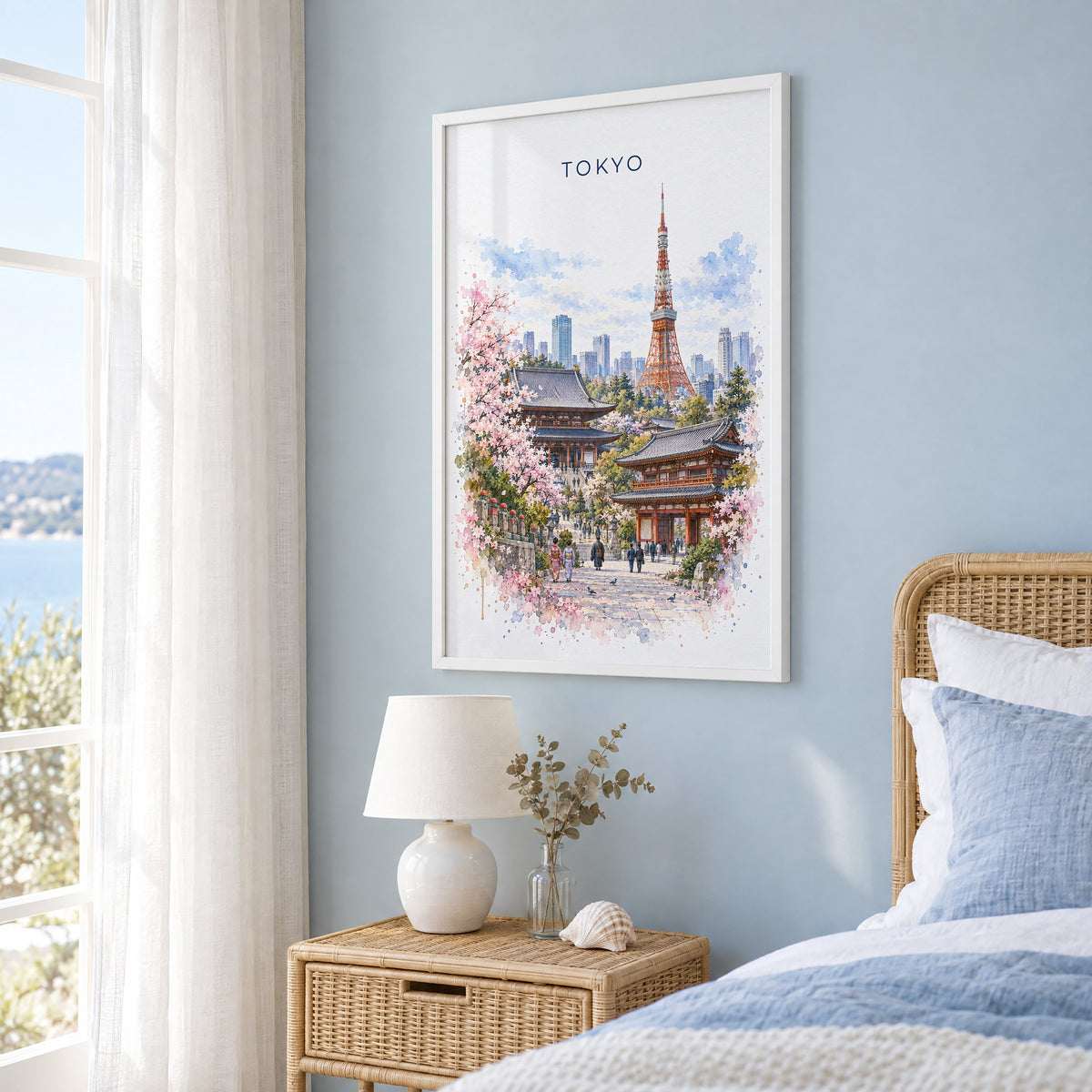 Tokyo watercolor print in a white frame on a pale blue wall beside a rattan bed in a coastal bedroom