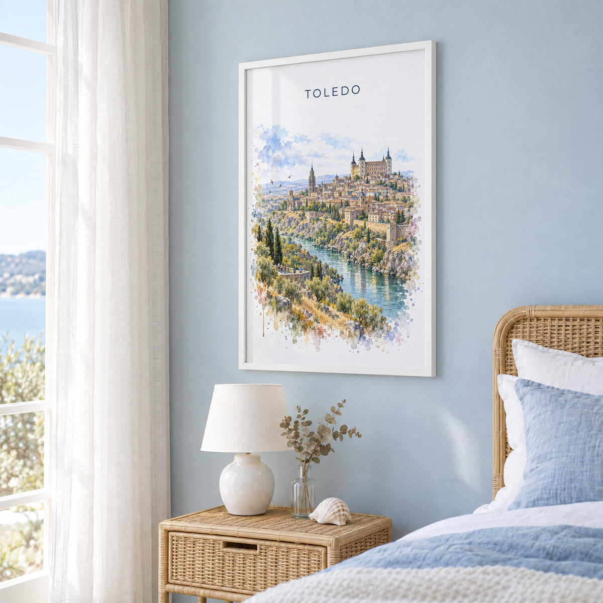 Toledo, Spain watercolor print in a white frame on a pale blue wall beside a rattan bed in a coastal bedroom