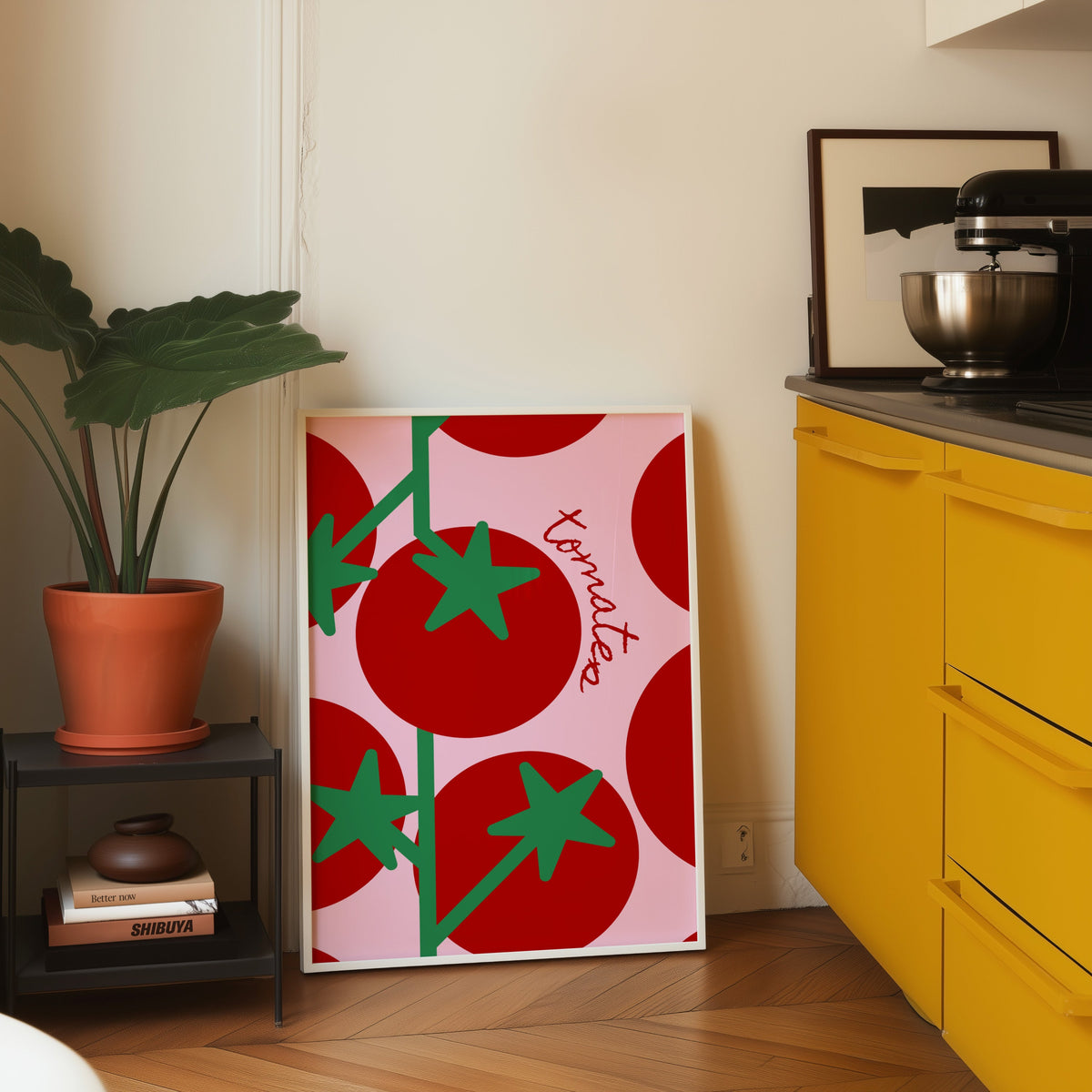 Tomates print in a white frame leaning on parquet beside a bright yellow kitchen