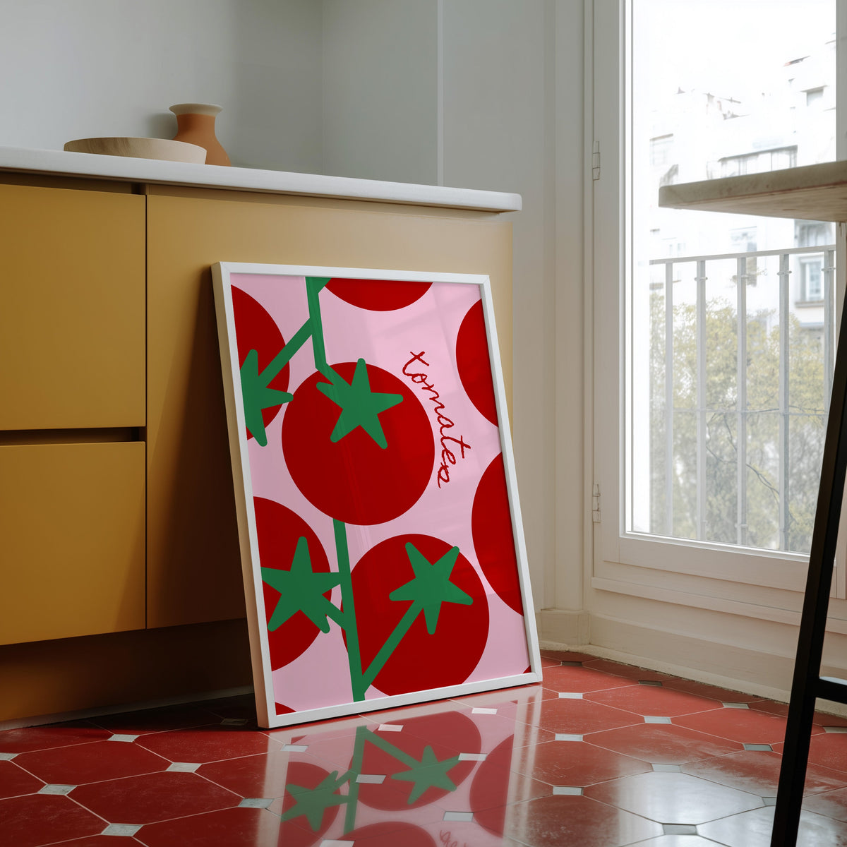 Tomates print in a white frame against yellow cabinets on a red tiled floor