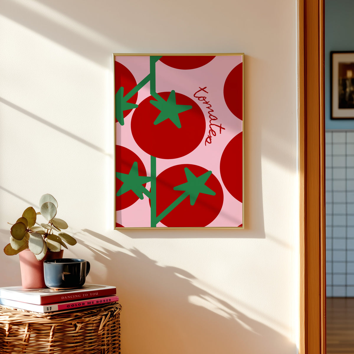 Tomates print in a gold frame above a basket of books and a pilea plant