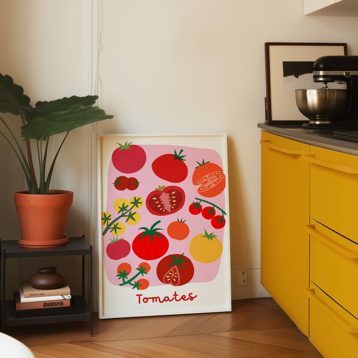 Tomates print in a white frame leaning on parquet beside a bright yellow kitchen
