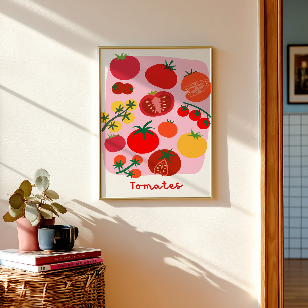 Tomates print shown in a gold frame above a basket of books and a pilea plant