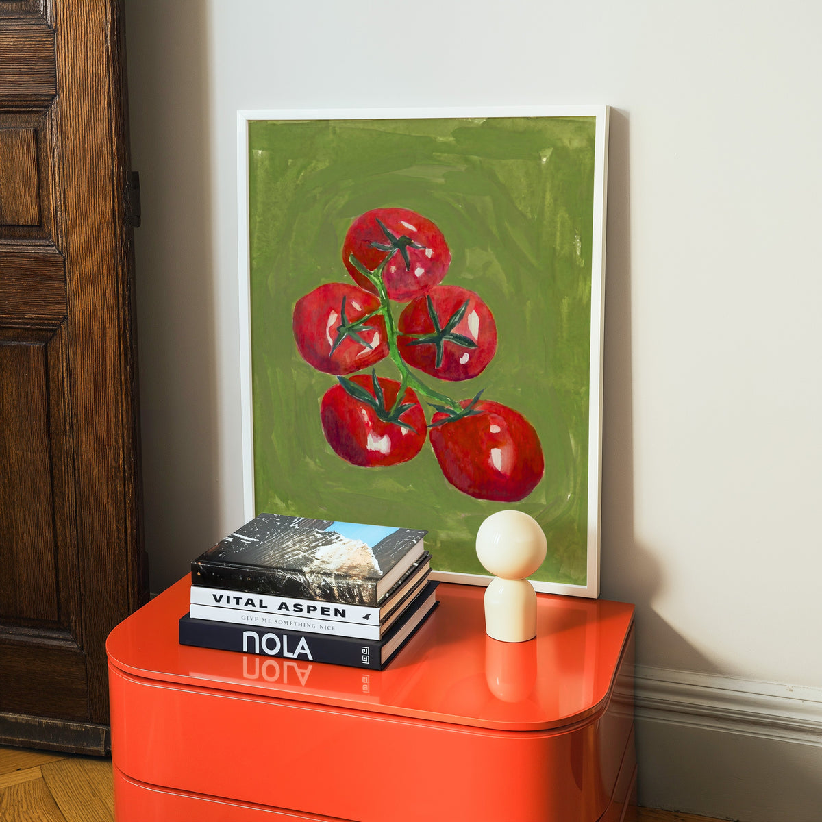 Farmers market tomato print in a white frame on a glossy orange cabinet with books