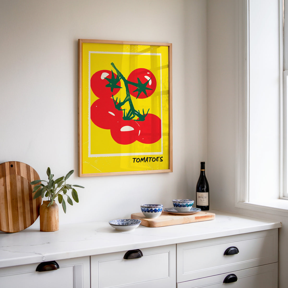 Tomatoes print in an oak frame above a white sideboard with a bottle of wine