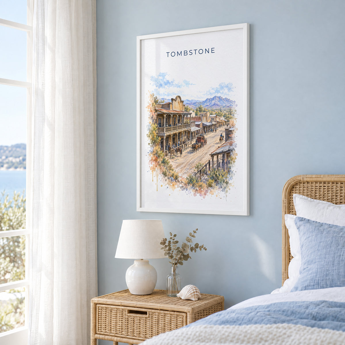 Tombstone, Arizona watercolor print in a white frame on a pale blue wall beside a rattan bed in a coastal bedroom