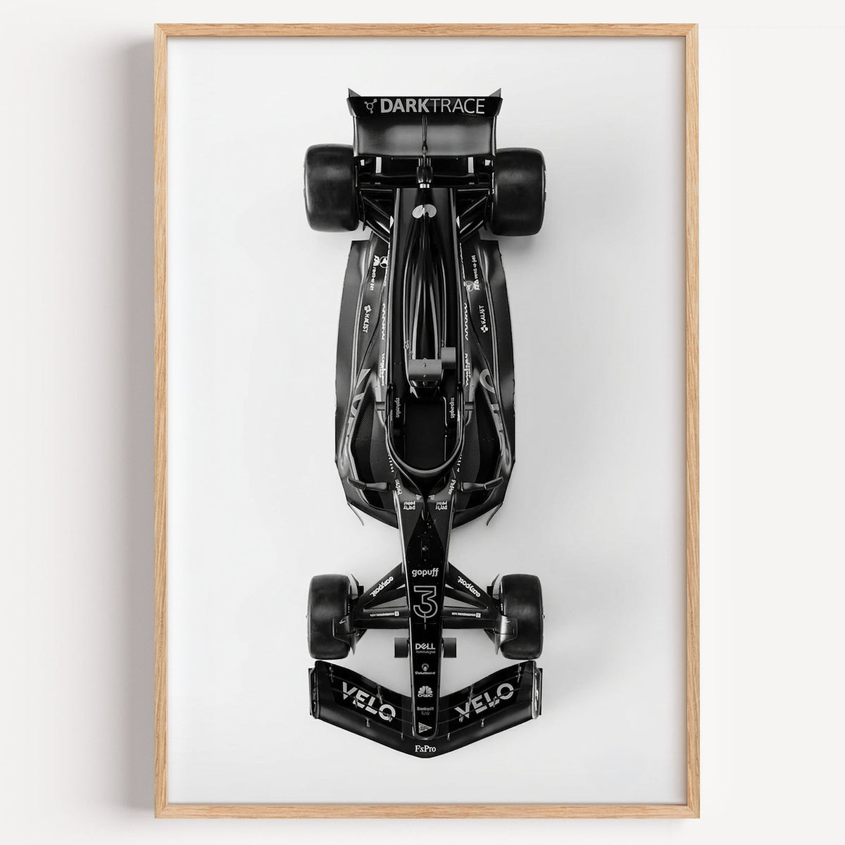 Top view black formula-style race car print in a light oak frame on a plain white wall