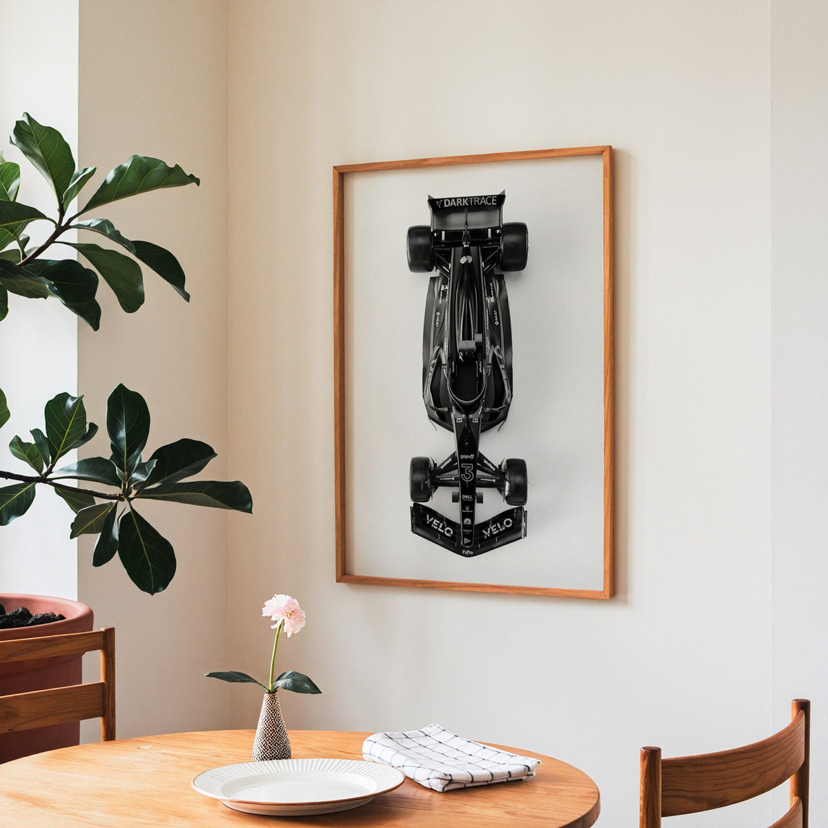 Top view black formula-style race car print in a teak frame above a round wooden dining table
