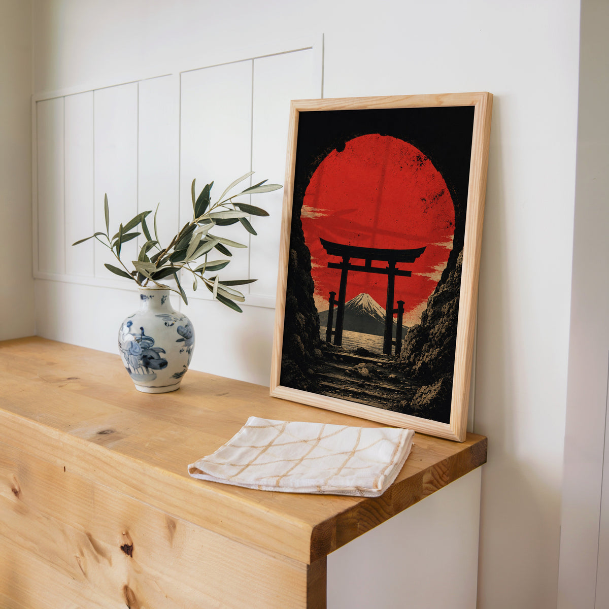 torii gate framing Mount Fuji and red sun print in a pine frame on a wooden counter beside a blue and white porcelain vase