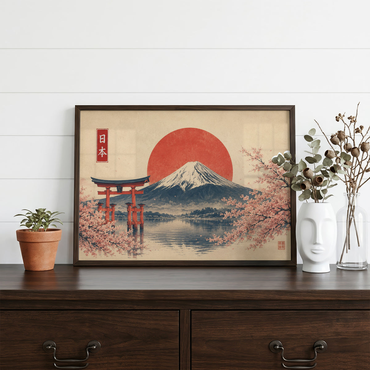 Torii gate and Mount Fuji with sakura print in a dark walnut frame on a dark wood dresser beside a white face vase