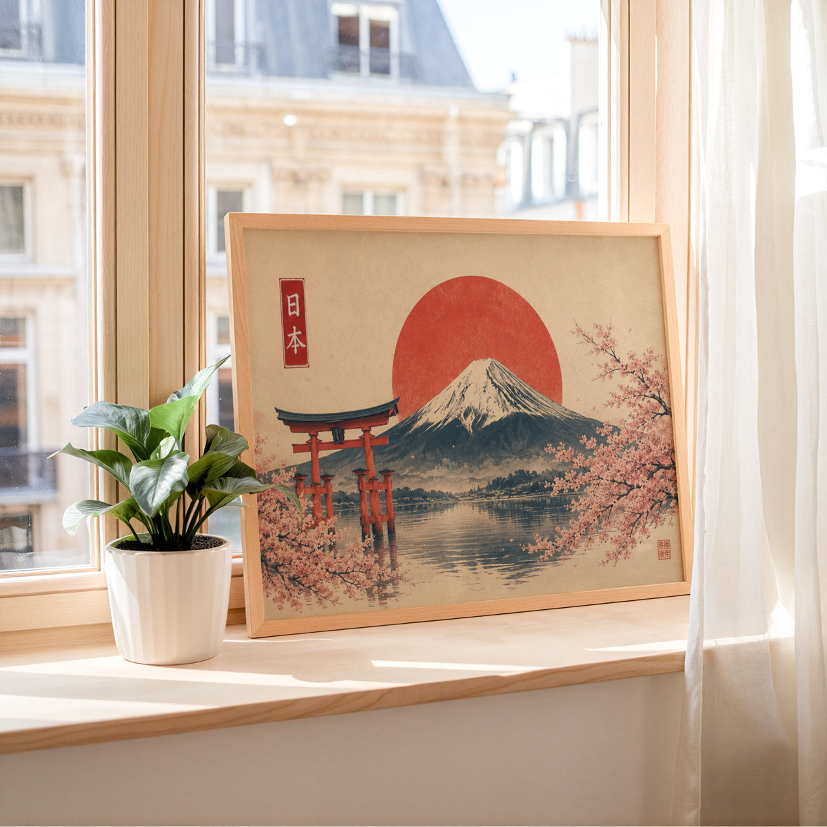 Torii gate and Mount Fuji with sakura print in a light wood frame leaning on a sunny windowsill by sheer curtains