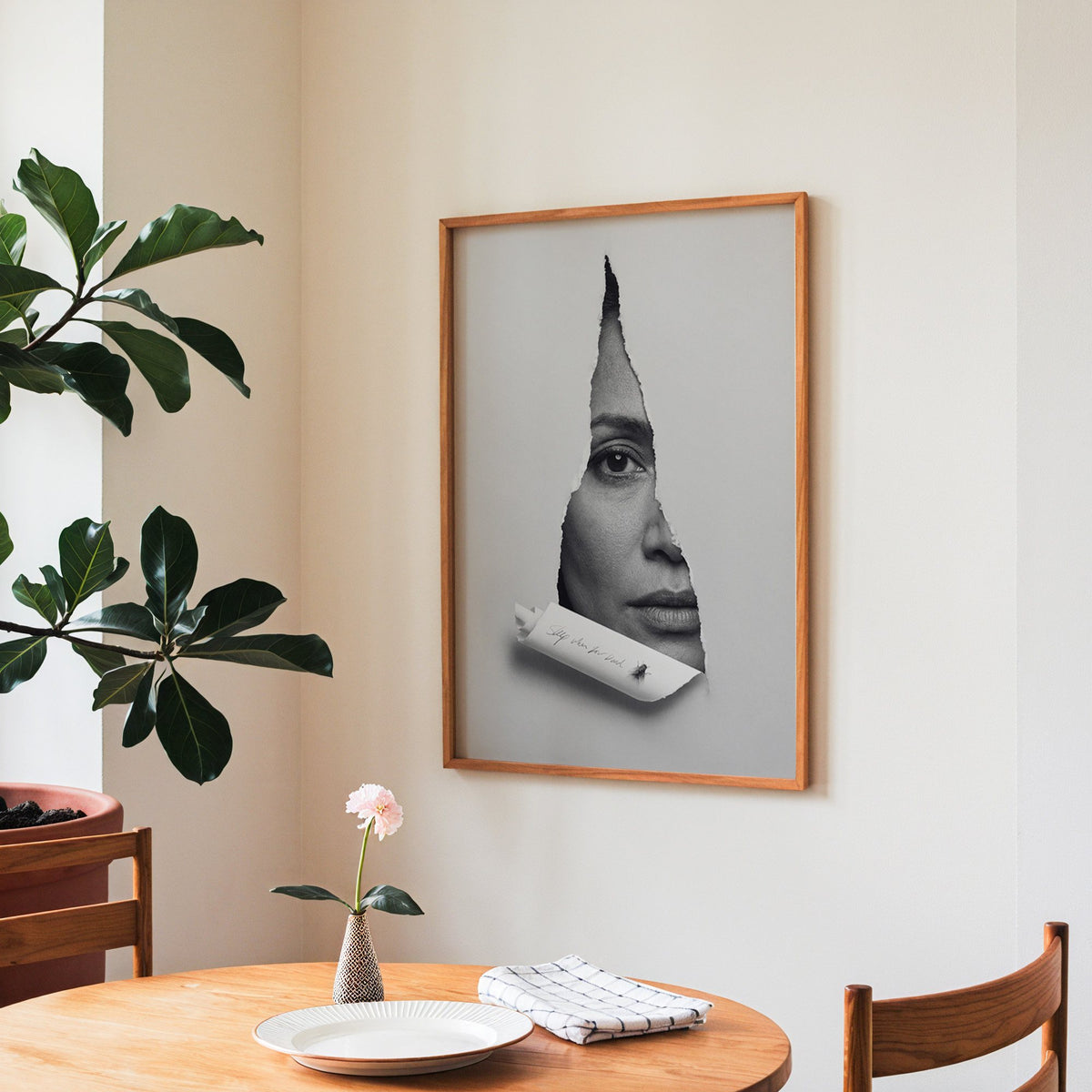 Half face behind torn grey paper slit print in a teak frame above a round wooden dining table