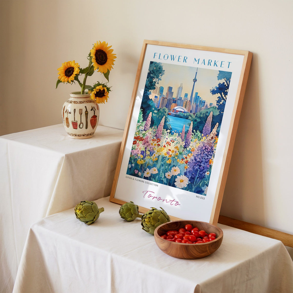 Toronto flower market print in an oak frame leaning on a linen-draped table beside a vase of sunflowers