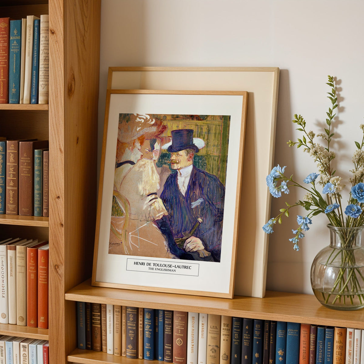 Man in a top hat print in an oak frame leaning on a bookshelf beside flowers