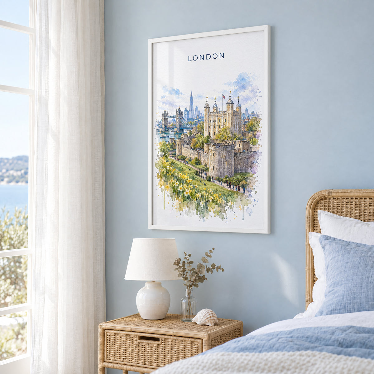 Tower of London watercolor print in a white frame on a pale blue wall beside a rattan bed in a coastal bedroom