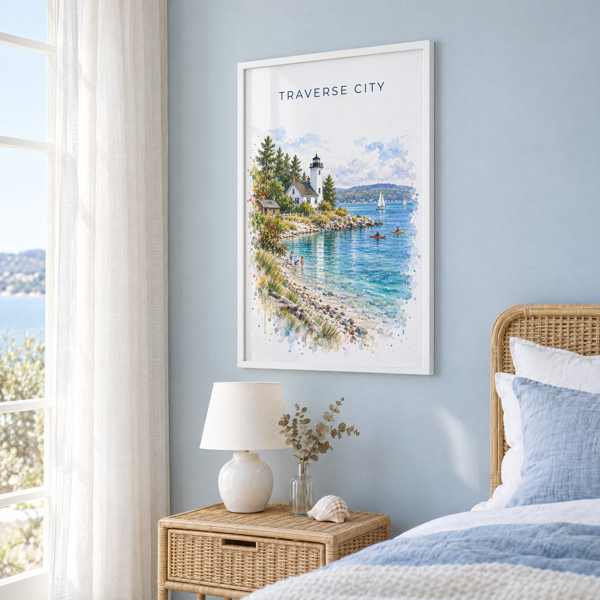 Traverse City watercolor print in a white frame on a pale blue wall beside a rattan bed in a coastal bedroom