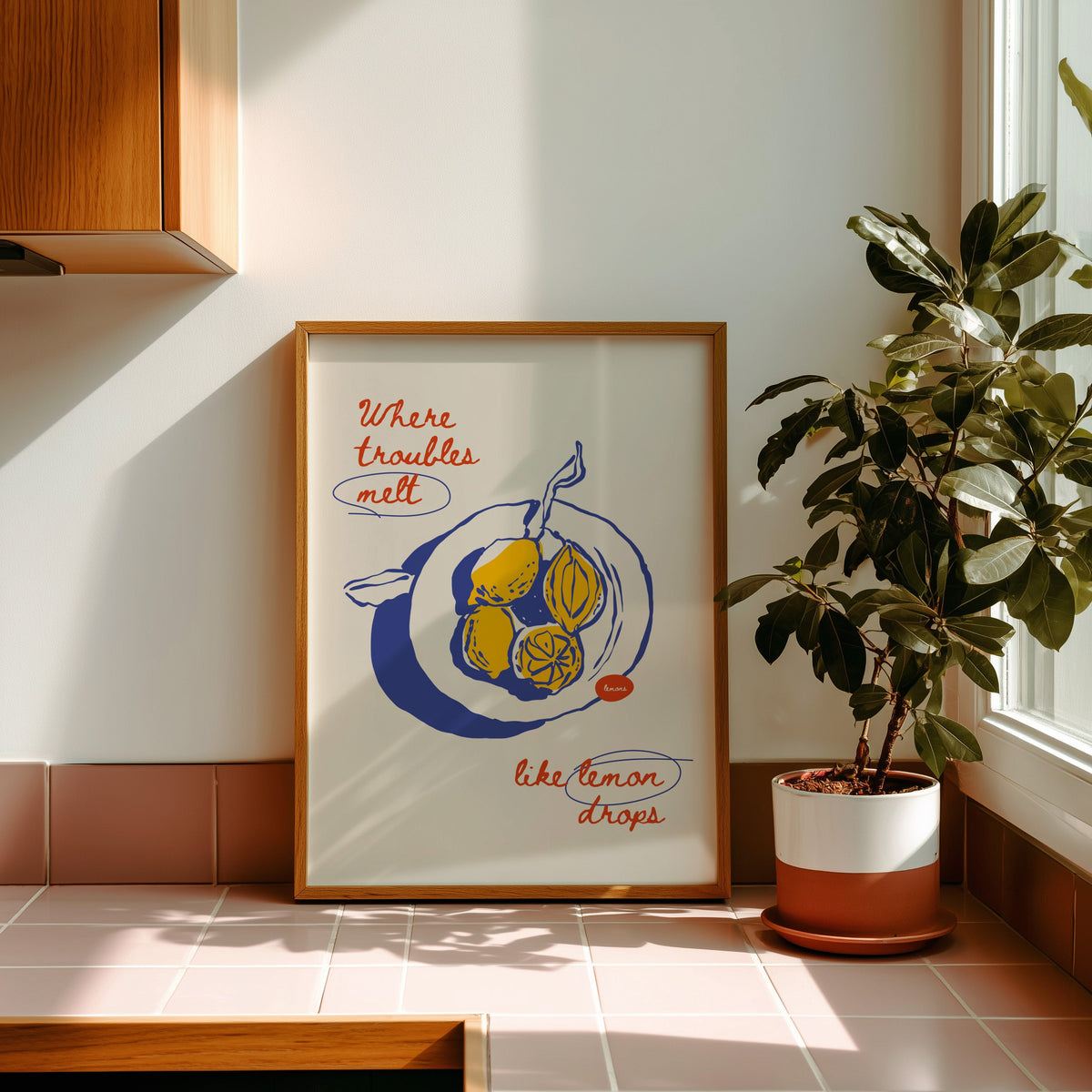 Lemon drops print in an oak frame on pink tiles in afternoon sun