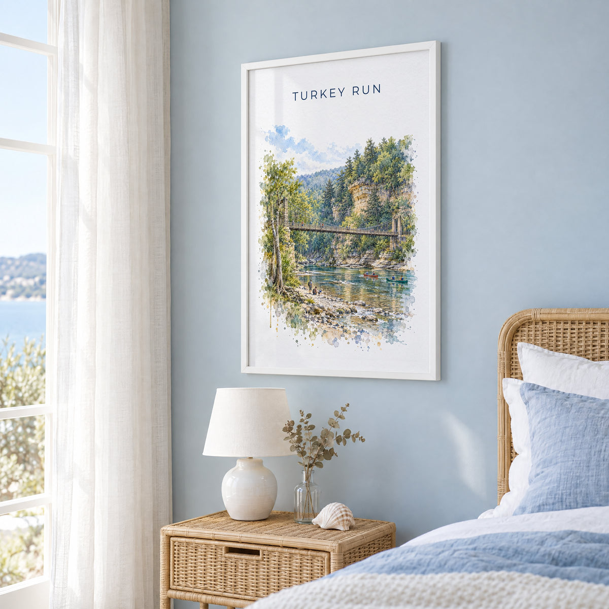 Turkey Run State Park watercolor print in a white frame on a pale blue wall beside a rattan bed in a coastal bedroom