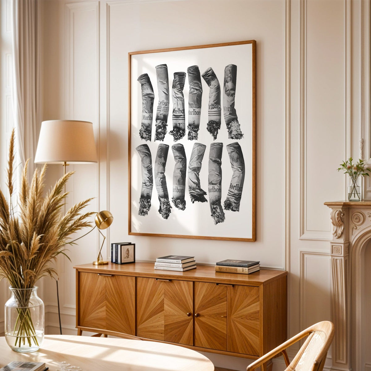 Twelve crushed cigarette ends in two rows print in an oak frame above a sunburst wood sideboard with pampas grass