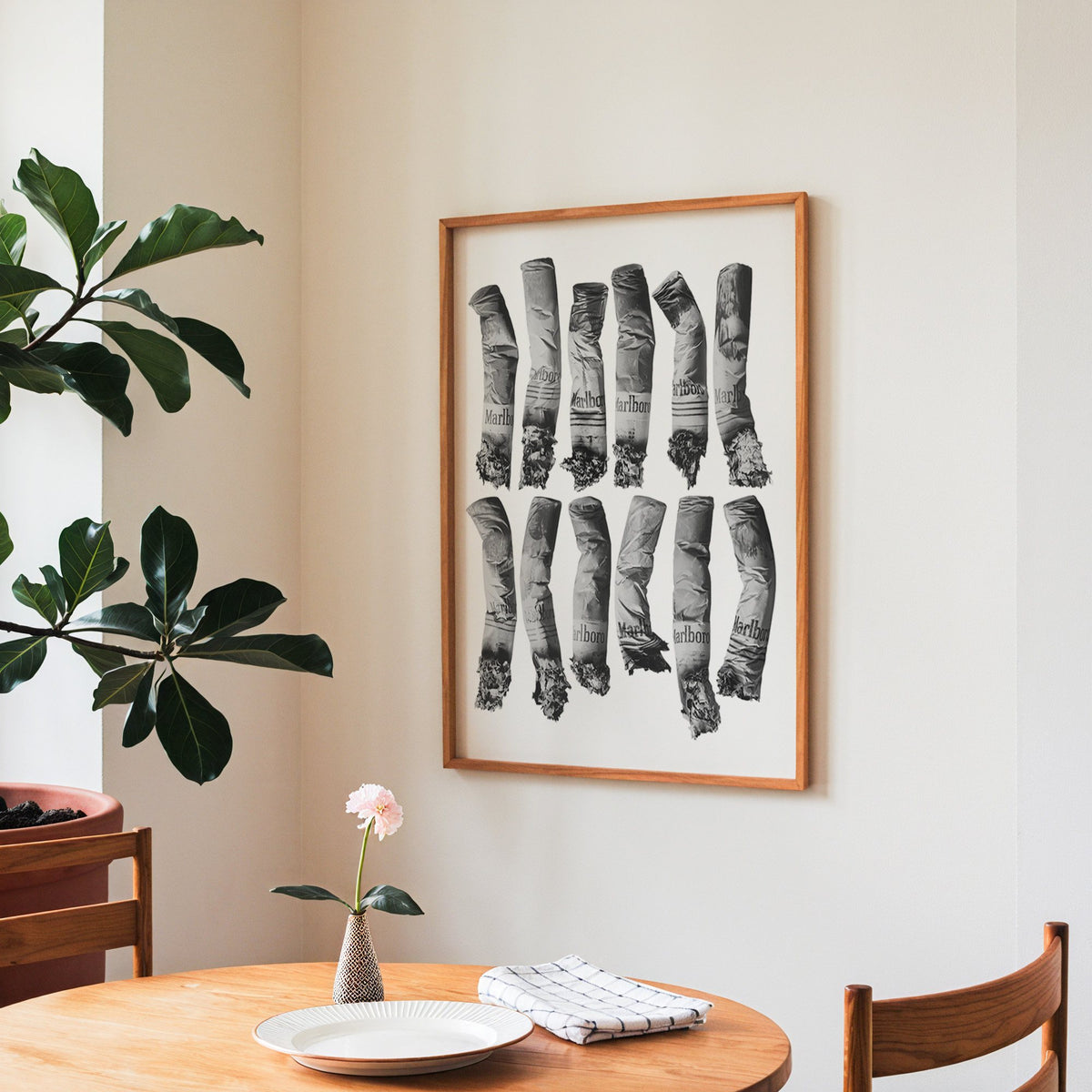 Twelve crushed cigarette ends in two rows print in a teak frame above a round wooden dining table