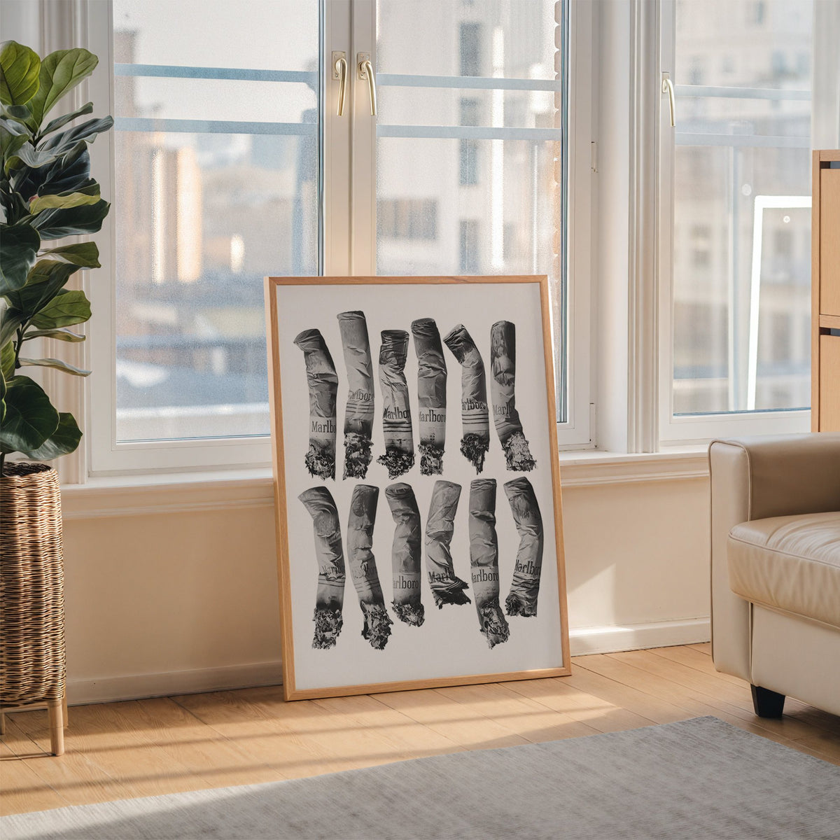 Twelve crushed cigarette ends in two rows print in an oak frame leaning on the floor beside a fiddle leaf fig