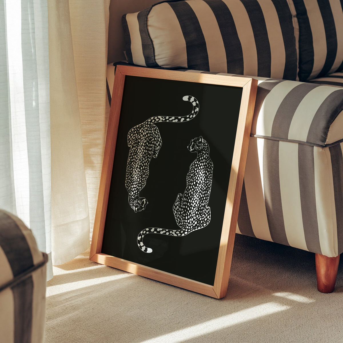 Twin cheetahs in white line art on black print in a pine frame leaning against a striped armchair