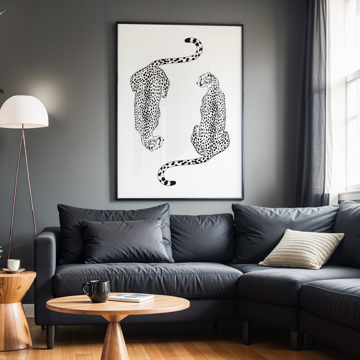 Two black line art cheetahs on white print in a black frame above a charcoal sofa on a grey wall