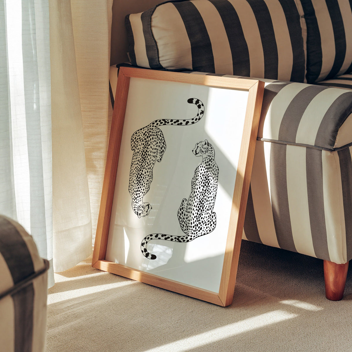 Two black line art cheetahs on white print in a pine frame leaning against a striped armchair