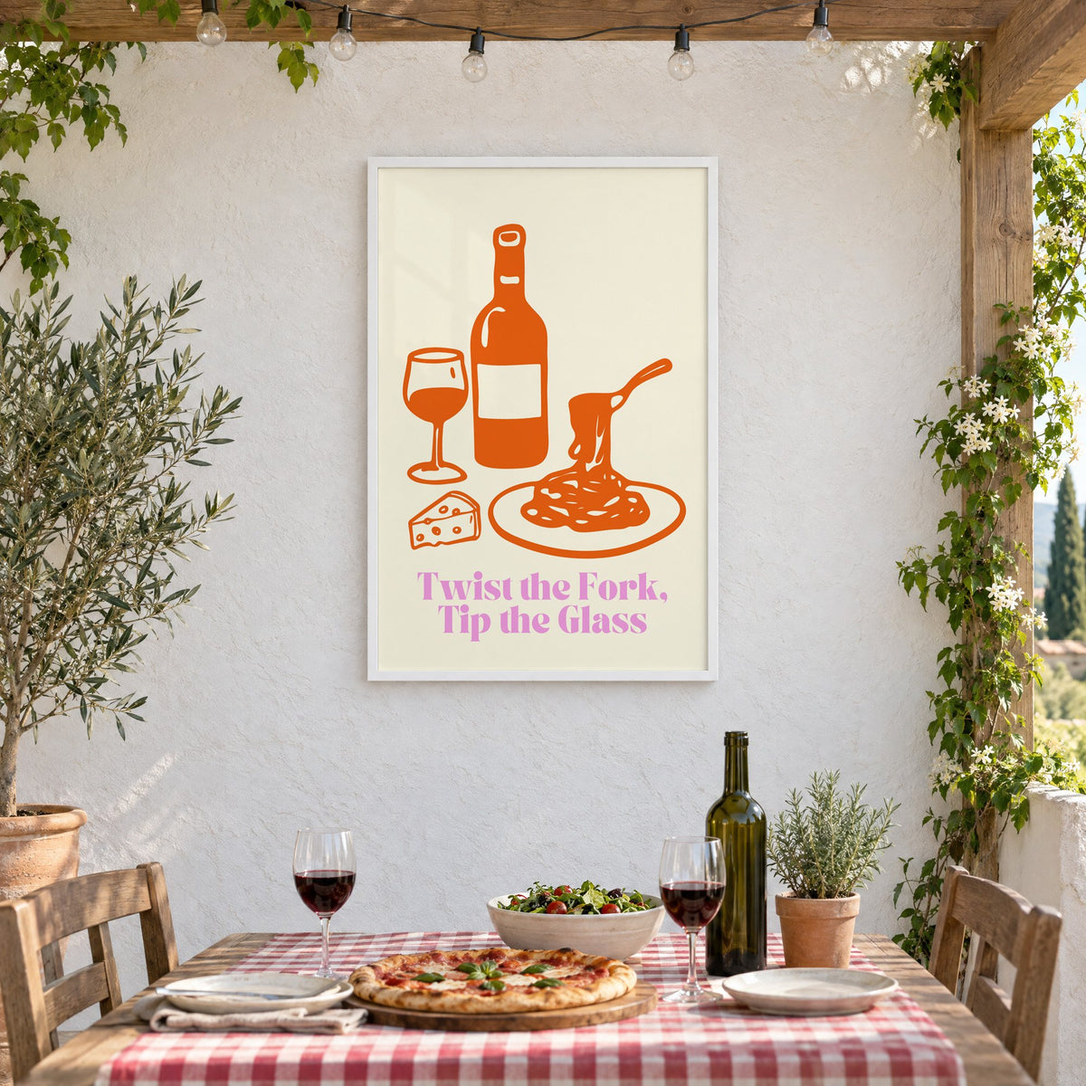 Twist the Fork, Tip the Glass wine and pasta print in a white frame on a stucco wall above a checked-cloth table with pizza and red wine