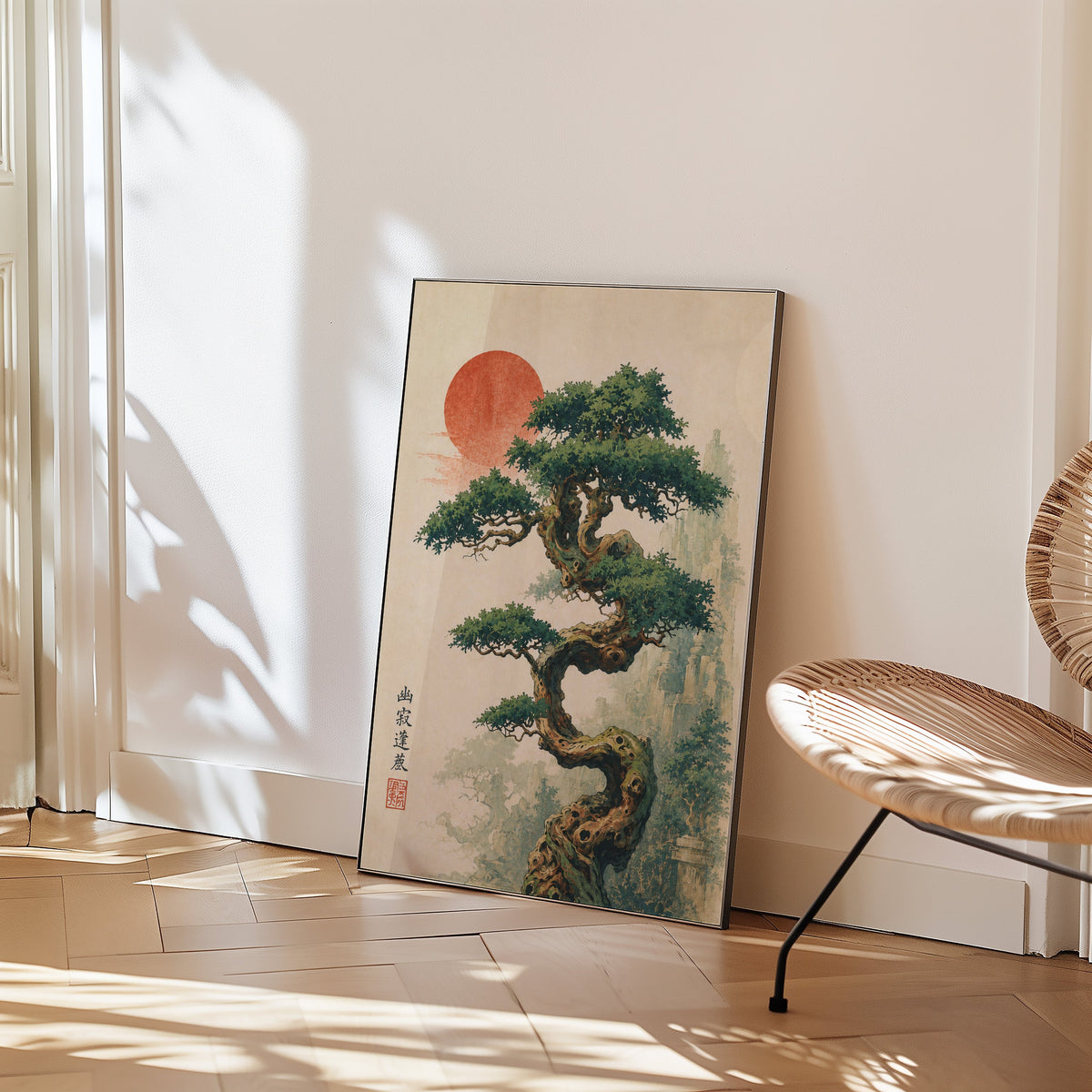 twisted bonsai tree with red sun print in a black frame leaning on a herringbone floor beside a woven rattan chair