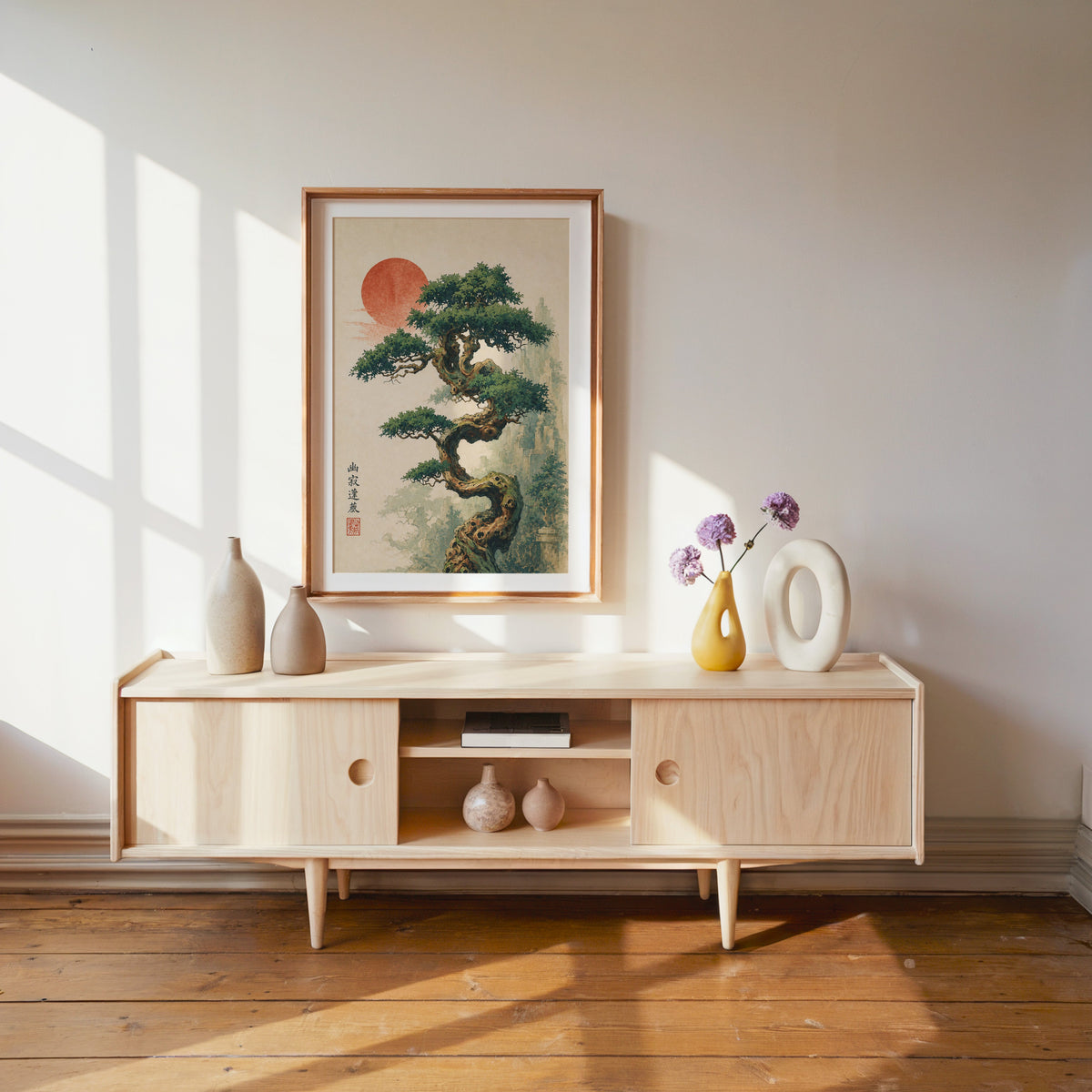 twisted bonsai tree with red sun print shown in a wood frame with a white mat above a pale wood media console