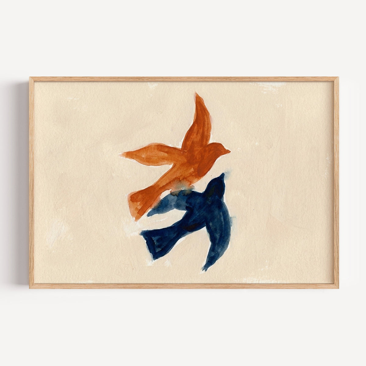 Two birds in flight watercolor print in a light oak frame on a plain white wall