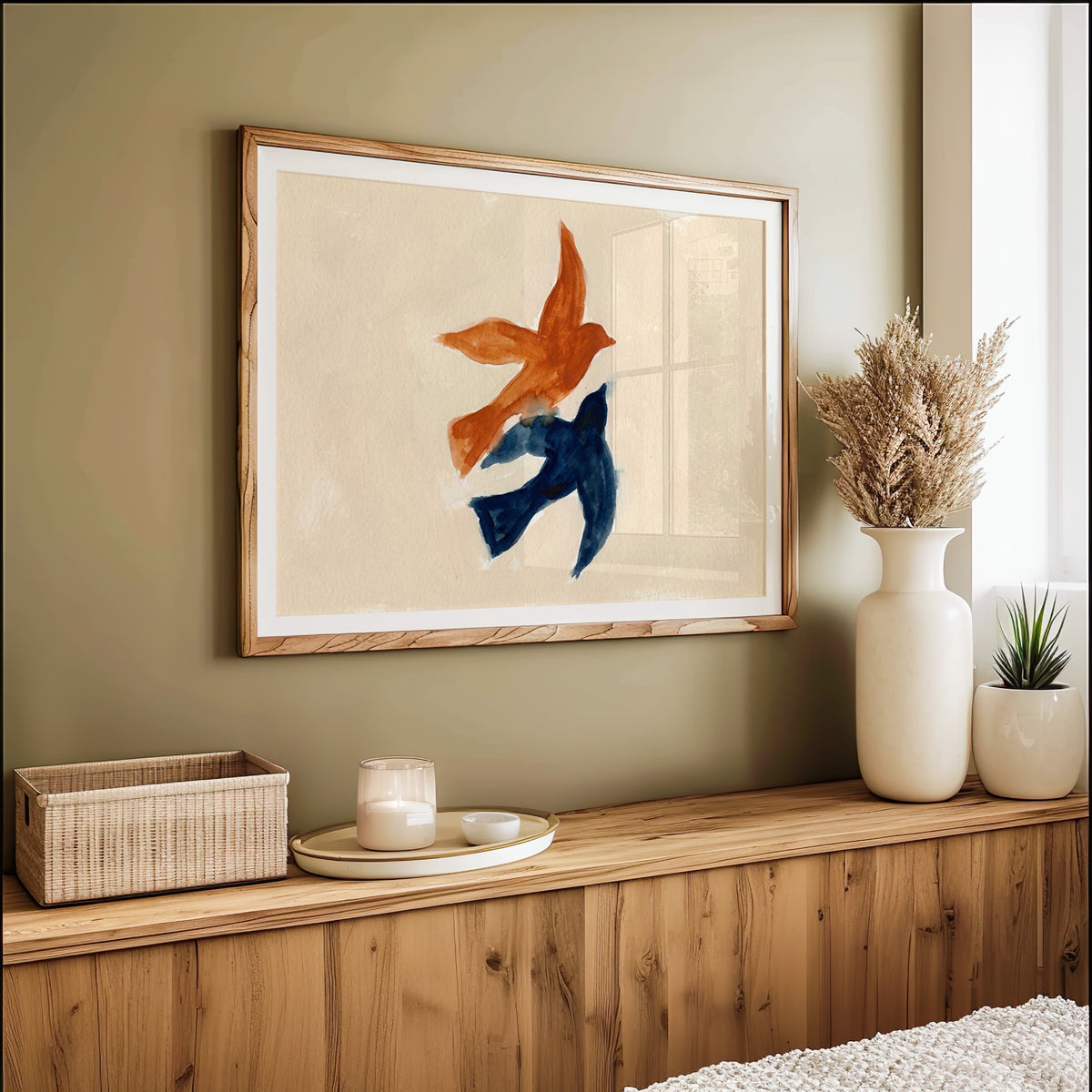 Two birds in flight watercolor print in an oak frame on an olive green wall above pampas grass