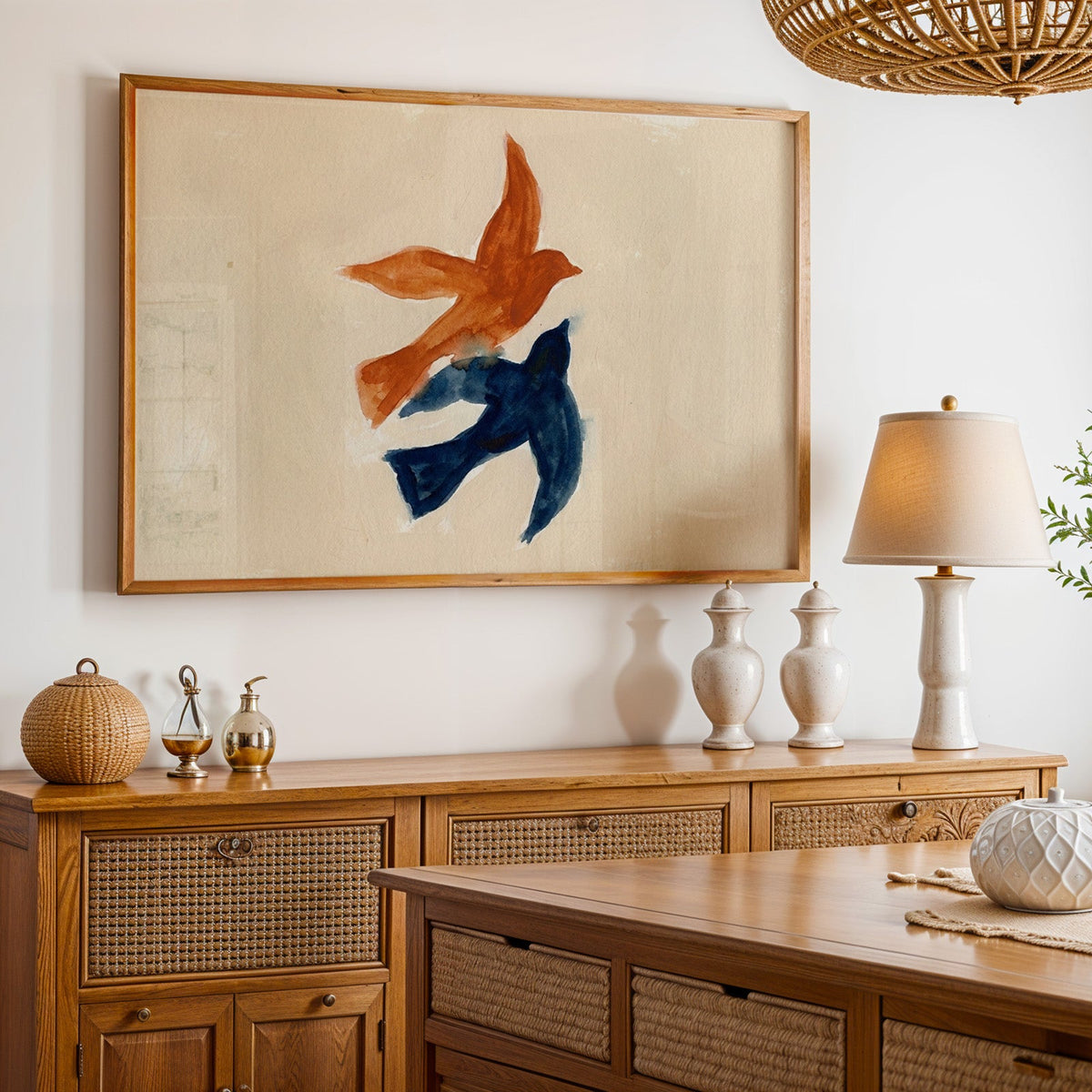 Rust and navy bird print in an oak frame above a cane sideboard with a table lamp