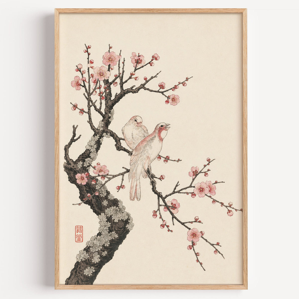 two birds on pink blossom branch print in a light oak frame on a plain white wall