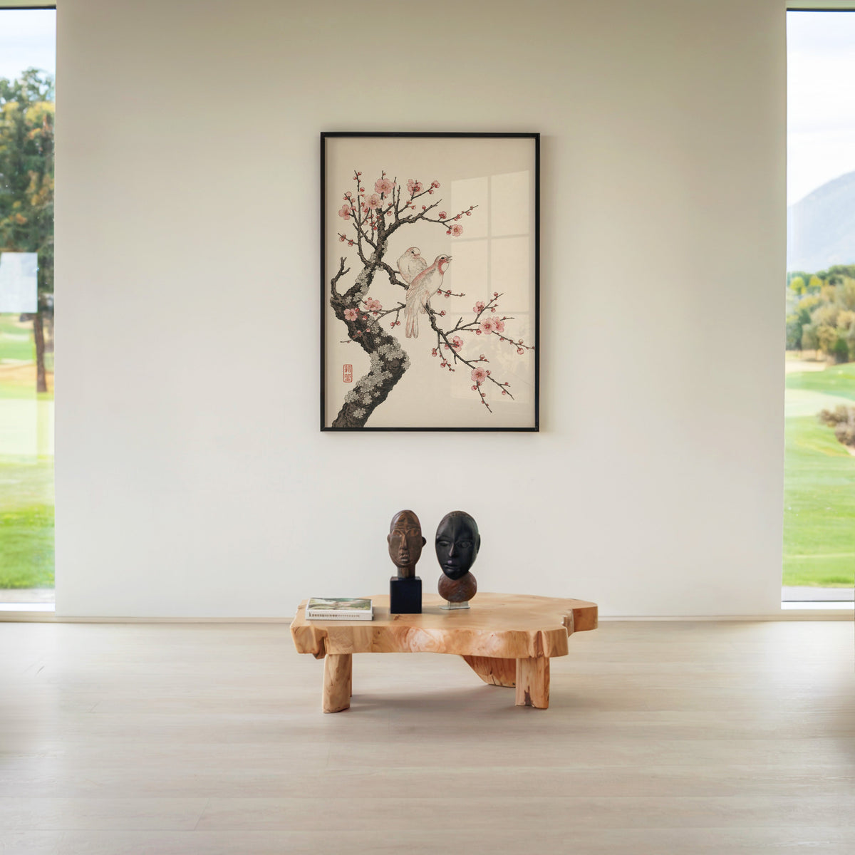two birds on pink blossom branch print in a black frame above a live-edge wood coffee table between garden windows